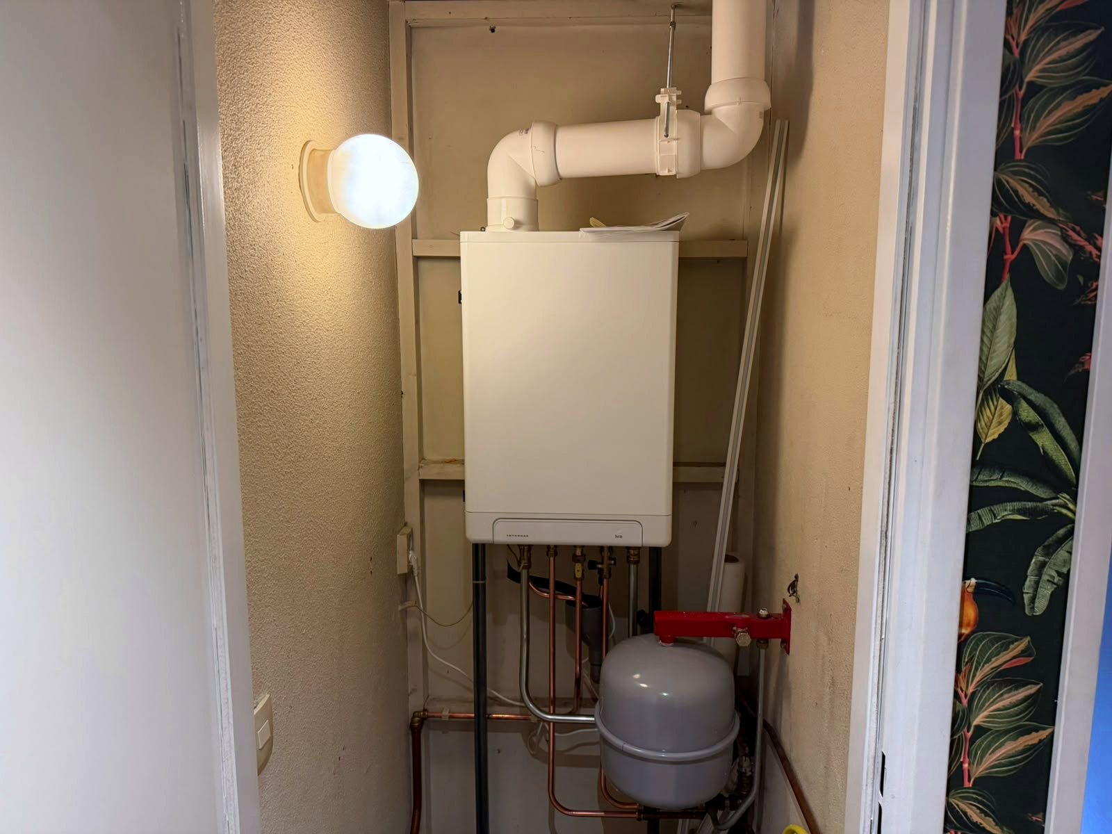 Intergas cv-ketel in een nis achter een deur, met een wit afvoerkanaal boven de ketel en een expansievat op een rode beugel