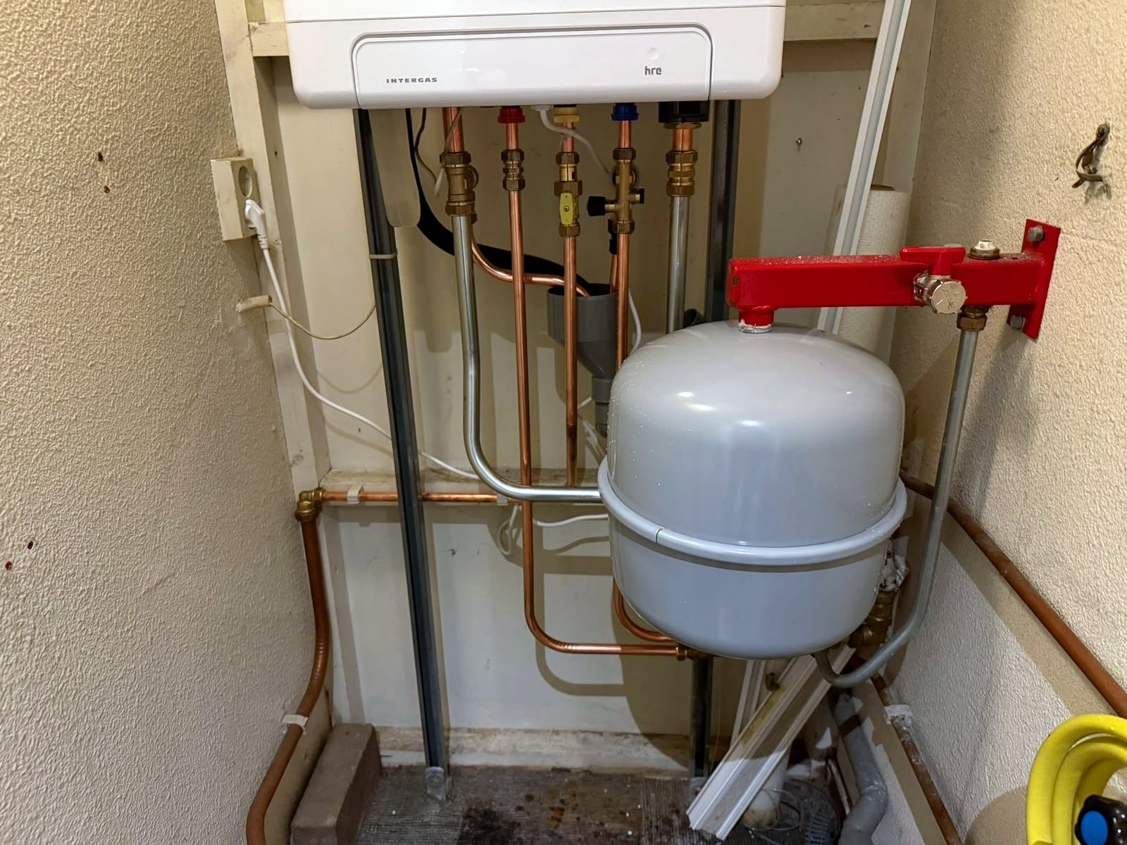 Detailfoto van de aansluitingen onder een Intergas cv-ketel, met koperen leidingen, messing kranen en een expansievat aan een rode beugel